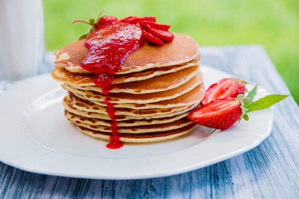 Pancakes with fresh strawberry and jam, near glass  milk on white plate   wooden background  in garden or  nature .  Stack of   the table. - Photo, Image