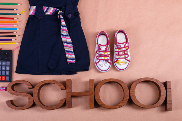 School uniform near sneakers and  supplies on orange background with an inscription . Top view, Copy space. outfit. Back to . - Photo, Image