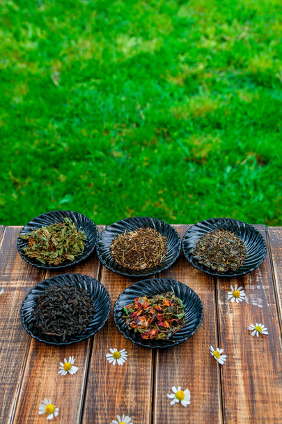 Различные виды чая на черных тарелках деревянный стол с цветами ромашки в саду и на фоне природы. Ассортимент сухой. концепция. листья. Крупный план
 - Фото, изображение