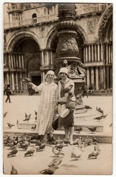 Vintage photo shows women feed the pigeons on the square in Venezia. Women wear cloche hats. Vacation theme. - Photo, Image