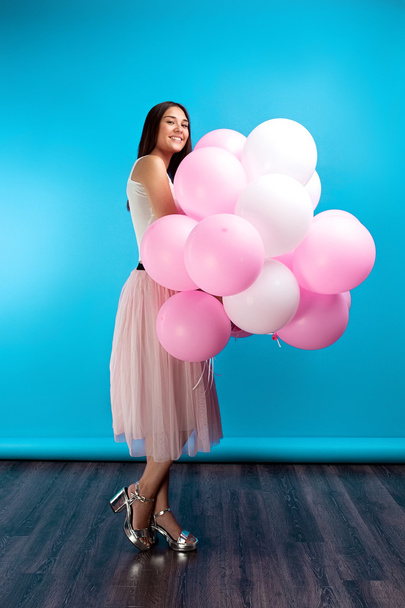 side view of cheerful and attractive girl with balloons smiling at camera on blue background.Studio shot - Foto, afbeelding