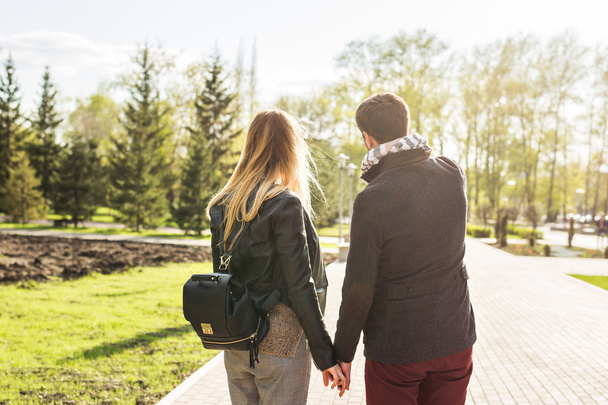 láska, vztahy, rodina a lidé koncept - mladý pár drží za ruce v podzimním parku zezadu - Fotografie, Obrázek