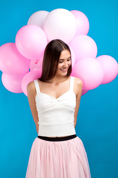 Portrait of cheerful smiling girl with pink balloons behind her looking down - Foto, afbeelding