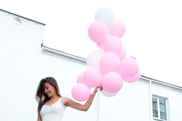 Low perspective of young brunette with pink balloons flying against of sky - Foto, Bild