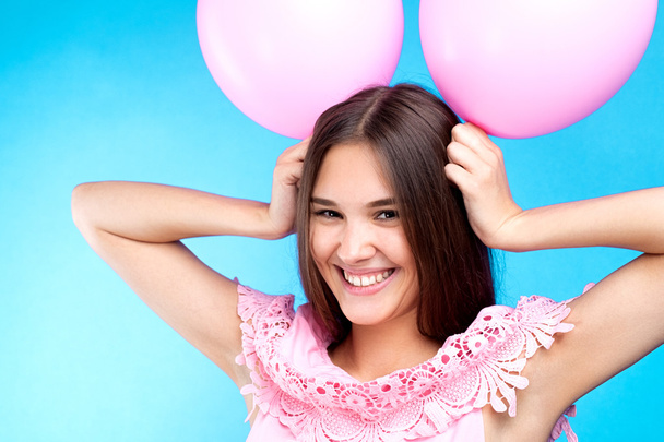 Funny young girl with pink balloons on head like minnie mouse smiling at camera.blue background - Photo, image