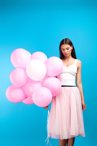 Conceptual shot of sad brunette girl with many pink balloons on blue background. - Fotoğraf, Görsel