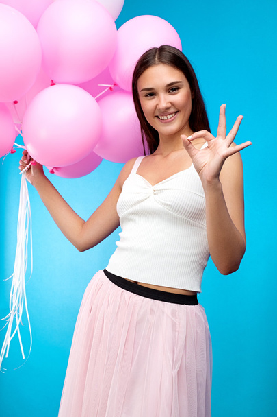 Portrait of attractive brunette smiling at camera with balloons and showing ok gesture - Foto, afbeelding