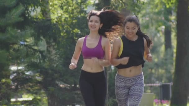 Dvě atraktivní Fitness sportovní mladé ženy s kudrnatými vlasy běží v parku na letní ráno, zpomalené - Záběry, video