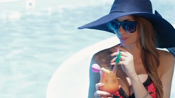 Woman holds a glass of cocktail in her hands near the swimming pool - Footage, Video
