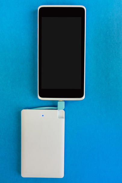 Smartphone charging with power bank on blue background - Foto, afbeelding
