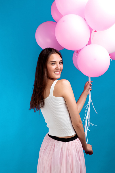 Rückseite der Brünette hält viele rosa Luftballons in der Hand und lächelt in die Kamera - Foto, Bild