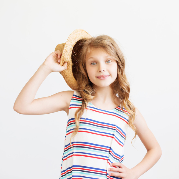 Милая маленькая девочка в соломенной шляпе и полосатом платье на белом фоне. Счастливые дети
 - Фото, изображение