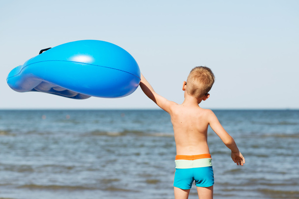 Little kid holding an inflatable mattress on the beach on hot su - Photo, Image