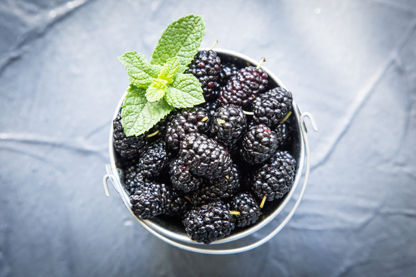 Свежая органическая черная тутовая ягода в маленькой корзине с листьями мяты
. - Фото, изображение