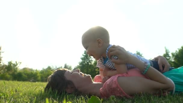 Young happy mother with a child lying and resting on a green lawn in a park - Footage, Video