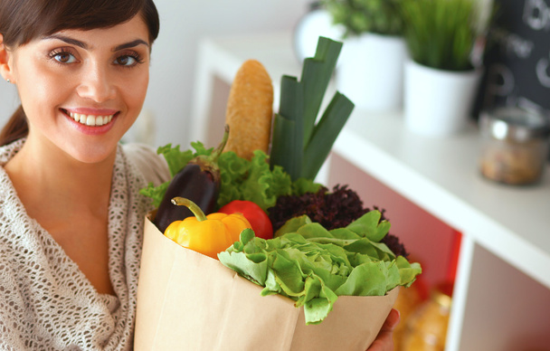 Young woman holding grocery shopping bag with vegetables Standing in the kitchen - Фото, изображение