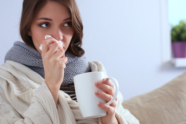 Portrait of a sick woman blowing her nose while sitting on the sofa - Photo, Image