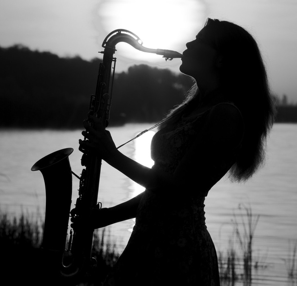 black and white portrait of beautiful girl playing the saxophone at the lake - Foto, Bild