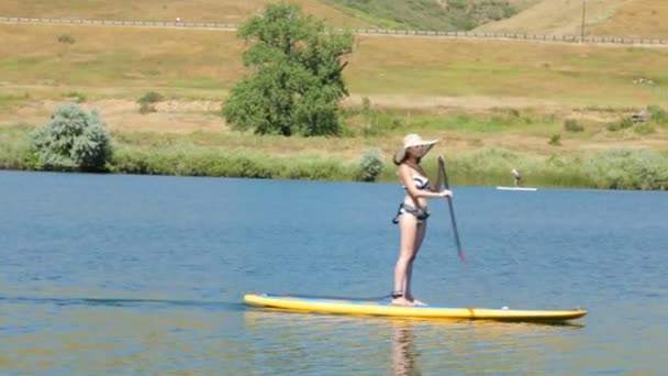 Νεαρή γυναίκα μαθαίνοντας πώς να paddleboard - Πλάνα, βίντεο