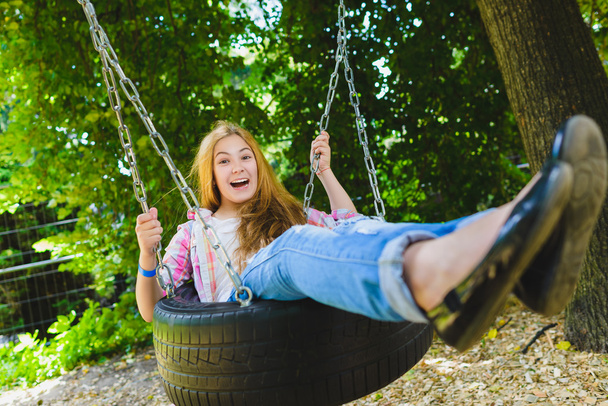 Uma menina no parque infantil. Criança brincando ao ar livre no verão. Adolescente em um balanço
. - Foto, Imagem