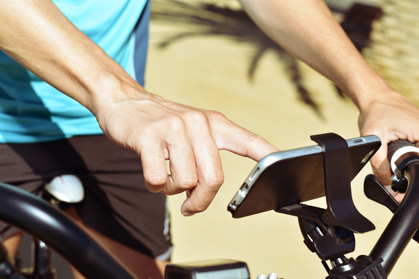 young man using a smartphone riding a bicycle - Zdjęcie, obraz