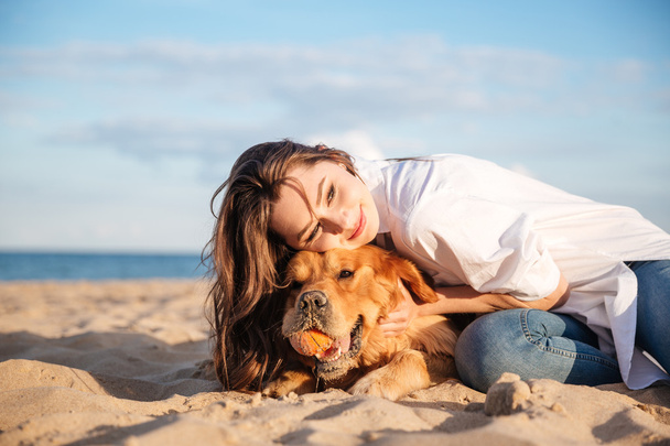 Smiling woman lying and hugging a dog on the beach - Foto, imagen