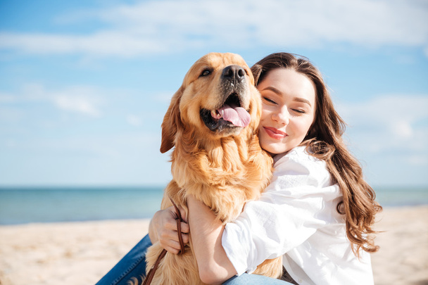 Tender smiling young woman hugging her dog on the beach - Φωτογραφία, εικόνα