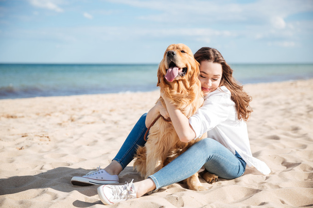 Happy woman sitting and hugging her dog on the beach - Фото, изображение
