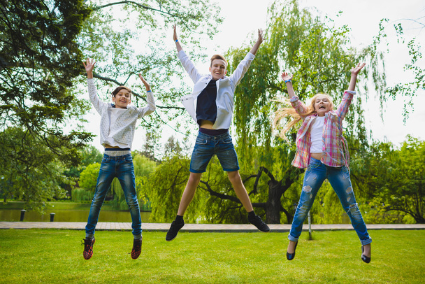 Улыбающиеся дети веселятся и прыгают по траве. Дети играют на открытом воздухе летом. подростки общаются на открытом воздухе
 - Фото, изображение