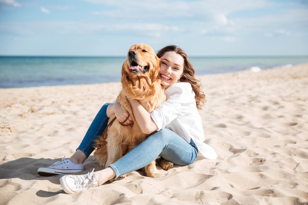 Happy woman sitting and hugging her dog on the beach - Fotoğraf, Görsel