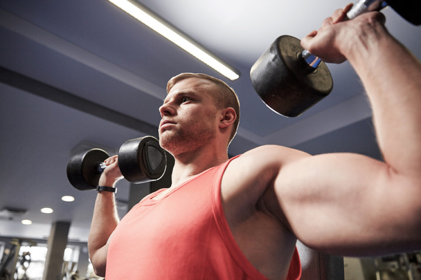 young man with dumbbells flexing muscles in gym - Fotoğraf, Görsel
