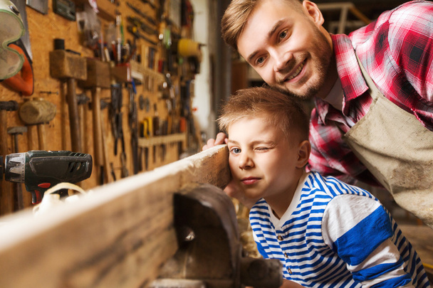 Vater und kleiner Sohn mit Holzplanke in Werkstatt - Foto, Bild