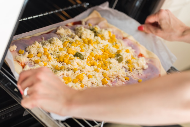 Τα χέρια της γυναίκας βάζοντας προετοιμασμένοι σπιτική πίτσα με ελιές, ζαμπόν, c - Φωτογραφία, εικόνα