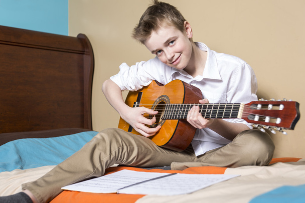 teini-ikäinen poika soittaa kitaraa hänen makuuhuoneessa
 - Valokuva, kuva