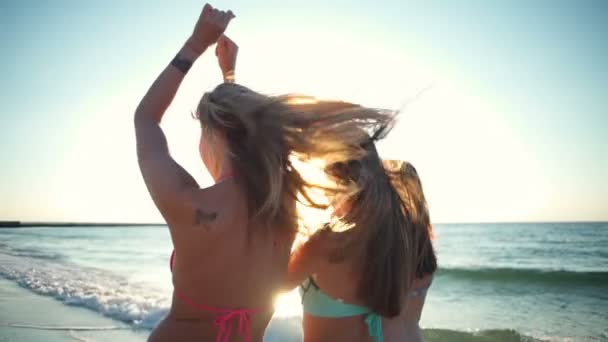 back view of three happy girls in bikini  walking along the sea slow motion - Felvétel, videó