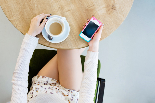 Girl's legs, cup of coffee and mobile phone - Photo, Image