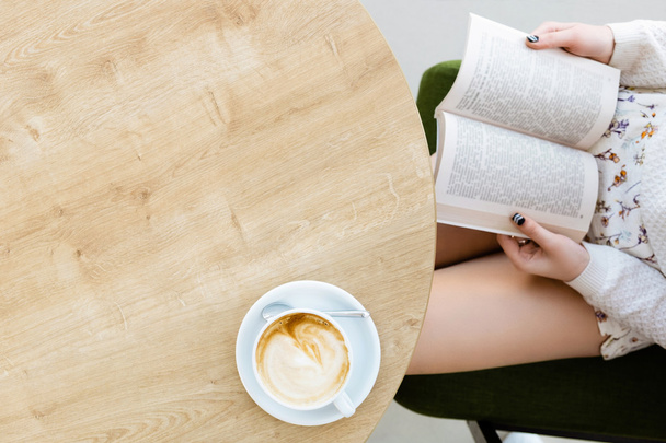 Pernas de menina, livro, xícara de café na mesa
 - Foto, Imagem