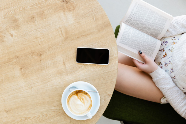 Girl's benen, kopje koffie, een boek en een mobiele telefoon - Foto, afbeelding