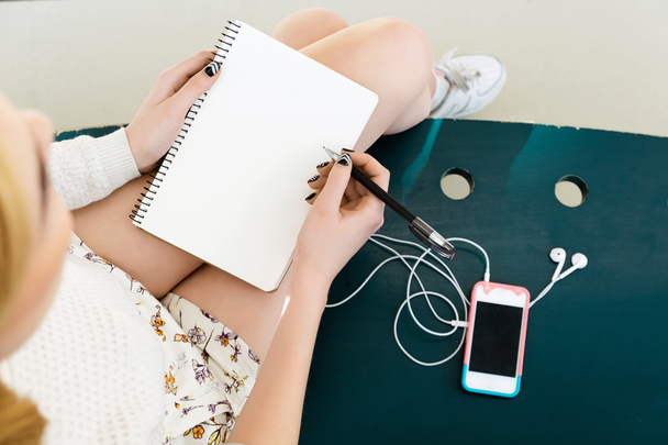Girl's benen, schrijven in notebook, mobiele telefoon - Foto, afbeelding