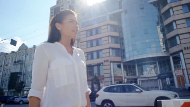 Vista lateral da mulher bonita em camisa branca e com cabelos longos escuros andando pelas ruas urbanas da cidade
 - Filmagem, Vídeo