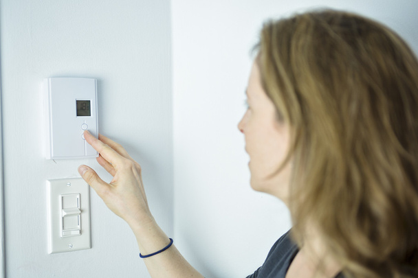 女性は家庭暖房システムでサーモスタットを調整します。 - 写真・画像