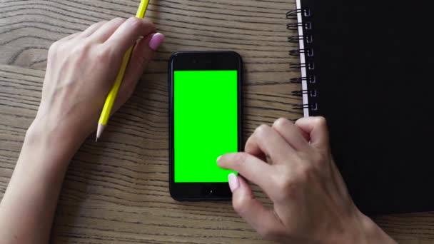 Θηλυκό χέρι χρησιμοποιώντας έξυπνο κινητό τηλέφωνο με μια πράσινη οθόνη σε ξύλινο τραπέζι, εναέρια θέα - Πλάνα, βίντεο