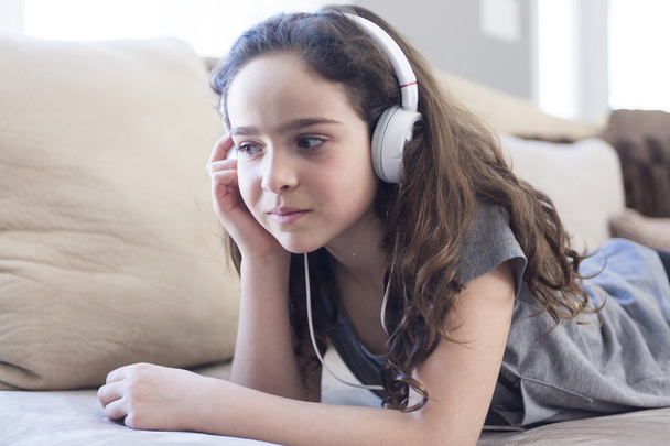 Woman listening music in headphones on sofa in room - Фото, изображение