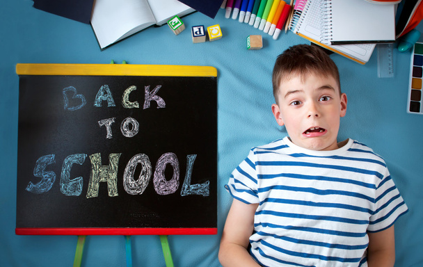 child lying on blue blanket with blackboard and school accessories - Photo, image