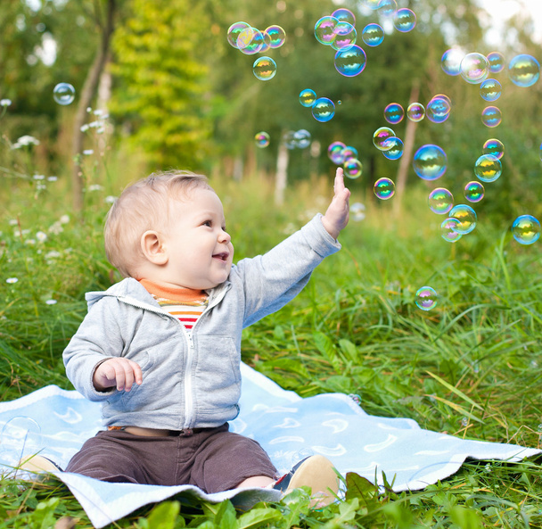 Boy sitting on green grass outdor playing with soap bubbles - 写真・画像