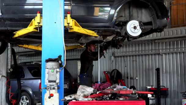 Reparaturarbeiter repariert Auspuffanlage an angehobener Limousine in Autowerkstatt - Filmmaterial, Video