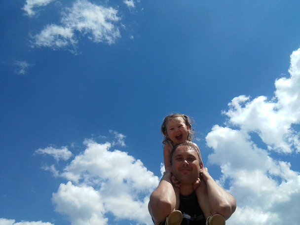 La hija feliz sobre sus hombros al padre contra el cielo
 - Foto, Imagen