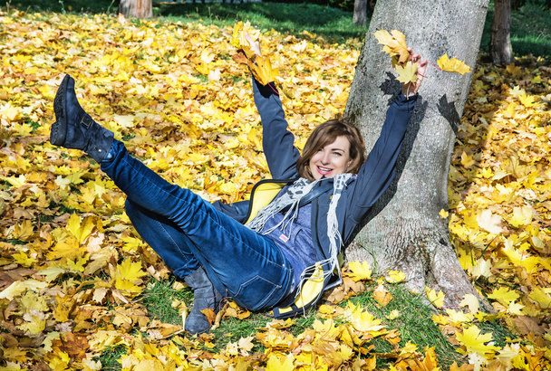 Τρελό νεαρή γυναίκα ρίχνει τα κίτρινα φύλλα το φθινόπωρο - Φωτογραφία, εικόνα