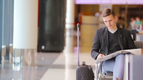 Kaukázusi fiatalember újság a repülőtéren, beszállás várva. Alkalmi fiatal üzletember viselt öltöny zakó. - Felvétel, videó