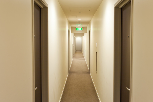 Corridoio lungo con porte della camera d'albergo e cartello di uscita
 - Foto, immagini